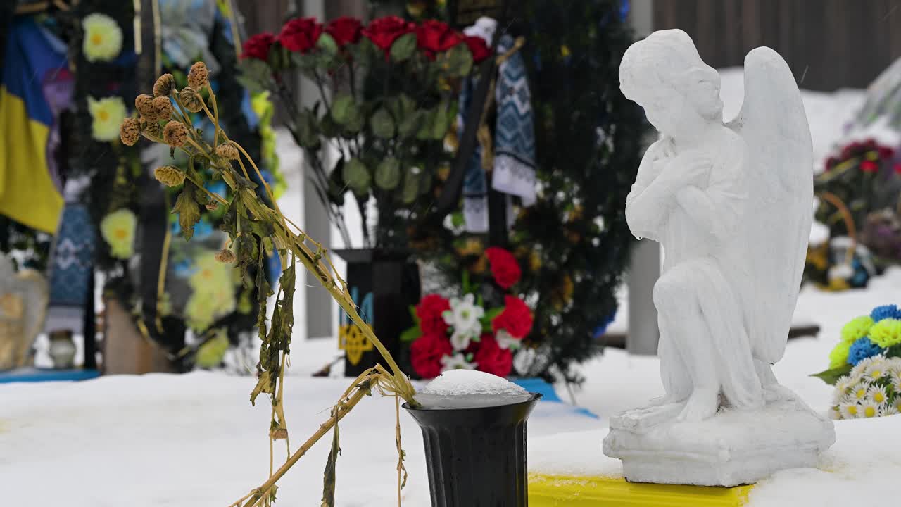 On a winter day, a close-up view of dying bouquet of flowers lies at the feet of an angel statue, paying tribute to a fallen Ukrainian soldier at Irpin Cemetery, Ukraine, from the Ukraine-Russia war.