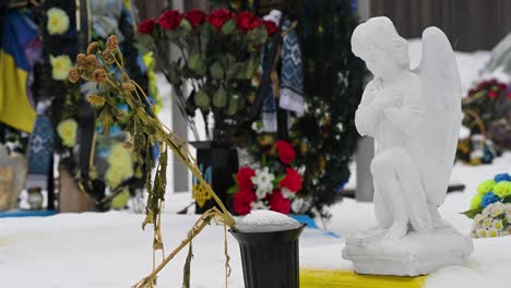 on a winter day, a close-up view of dying bouquet of flowers lies at the feet of an angel statue, paying tribute to a fallen ukrainian soldier at irpin cemetery, ukraine, from the ukraine-russia war.