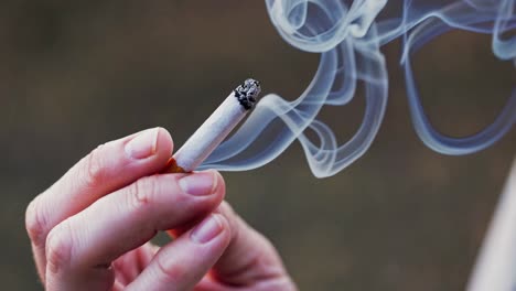 close-up video shot of a hand holding a lit cigarette, with smoke swirling upward