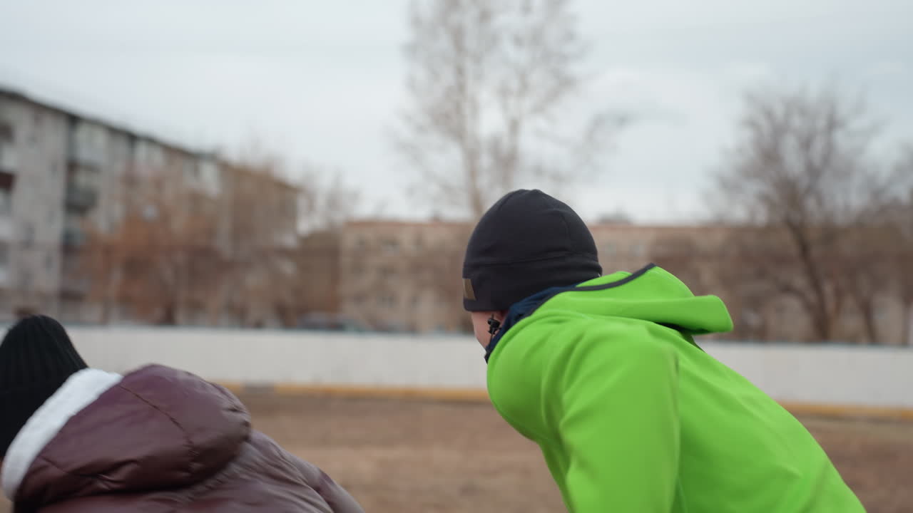 도시 건물 근처 초목을 지나 즐겁게 질주하는 모습, 야외에서 남자와 여자가 활기차게 게임을 하는 모습, 흐린 날 아파트 단지를 배경으로 탁 트인 들판에서 생동감 넘치는 추격전