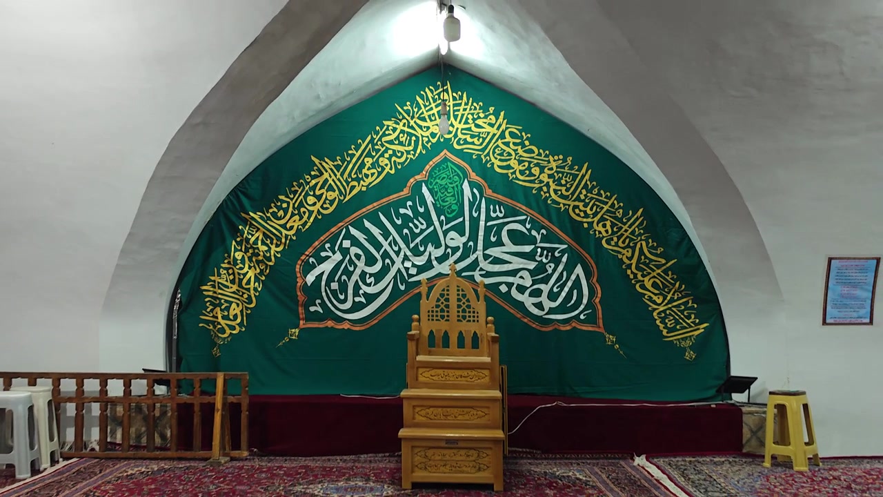 Mimbar Kayu di Depan Spanduk Kaligrafi Hijau di Masjid