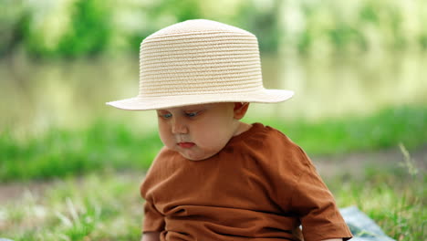 funny little baby boy wearing mom's hat sits outdoors. cute child in the nature in summer. close up.