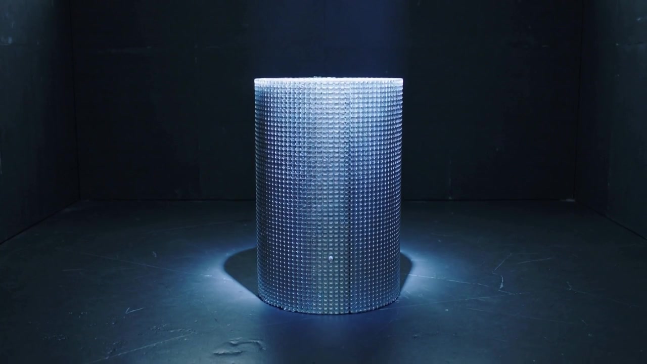Skinnende spotlight afslører tekstureret cylinder i mørkt kammer, strålen udvides og blotlægger cirkulært gitter.