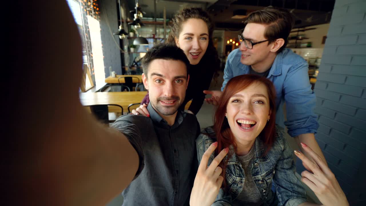 Ripresa in soggettiva di un allegro gruppo di amici che registra un video divertente in un caffè, posando, sorridendo, abbracciandosi e gesticolando. Concetto di amicizia e persone felici