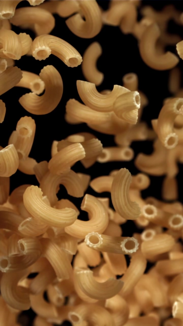 Pasta maccheroni secca che cade al rallentatore su sfondo nero.