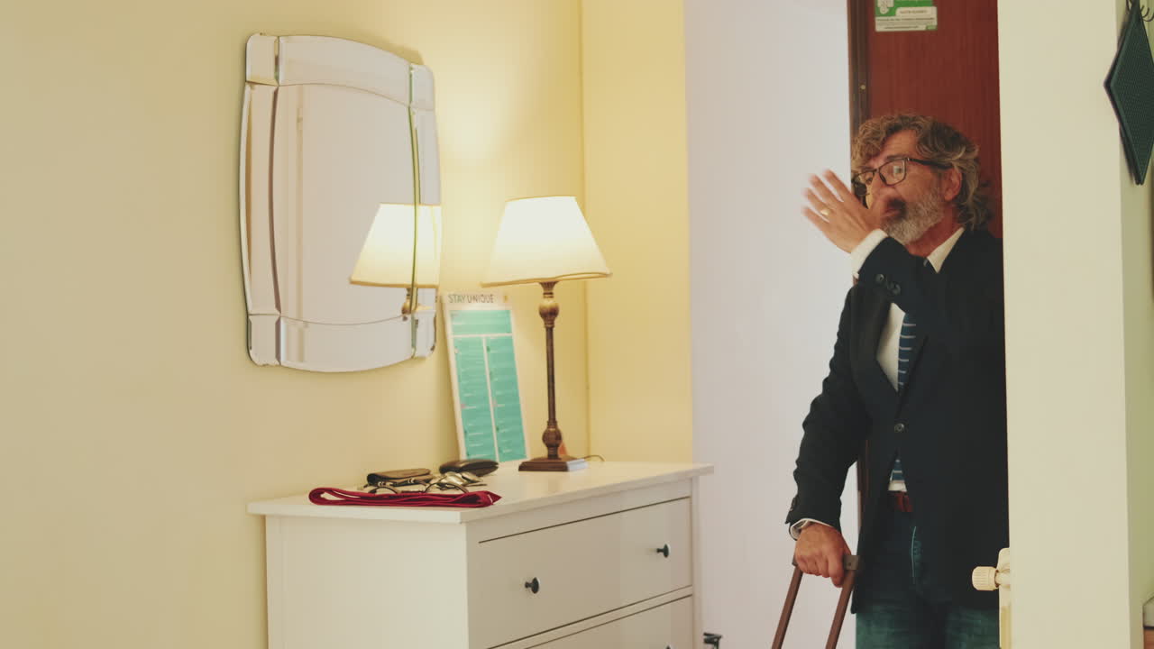 A man in a suit waves goodbye in a hotel room