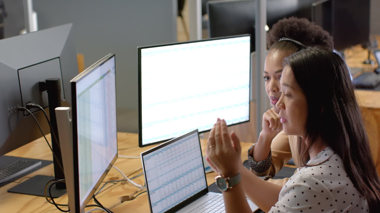 dos mujeres de negocios, una biracial y una afroamericana, revisan un rastreador de ventas en una pantalla