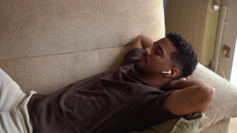 calm ethnic man sleeping in earphones on sofa