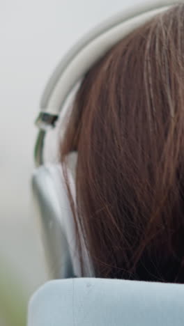 closeup head view of lady wearing headphones, showcasing her hair and the headset, peaceful outdoor moment, focused expression, enjoying music, urban setting with blurred background