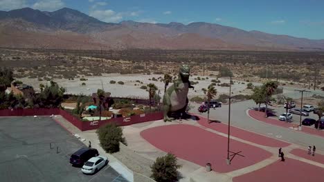 aerial over a giant artifical dinosaur looming over visitors as a roadside attraction in the mojave desert near cabazon california