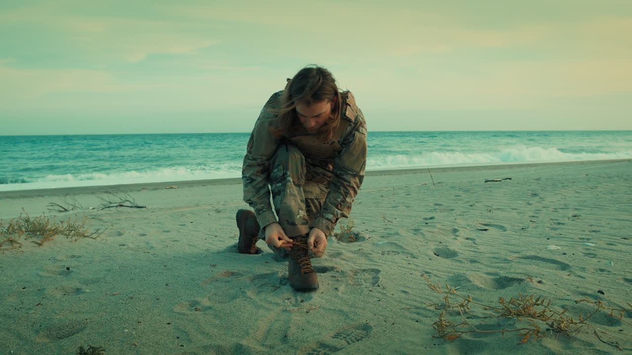 Un militare della Marina si allaccia le scarpe anfibie sulla spiaggia vicino all'oceano