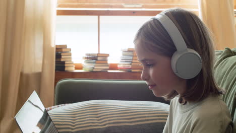 Primer-Plano-De-Una-Niña-Rubia-Feliz-Con-Auriculares-Mirando-La-Pantalla-Del-Portátil