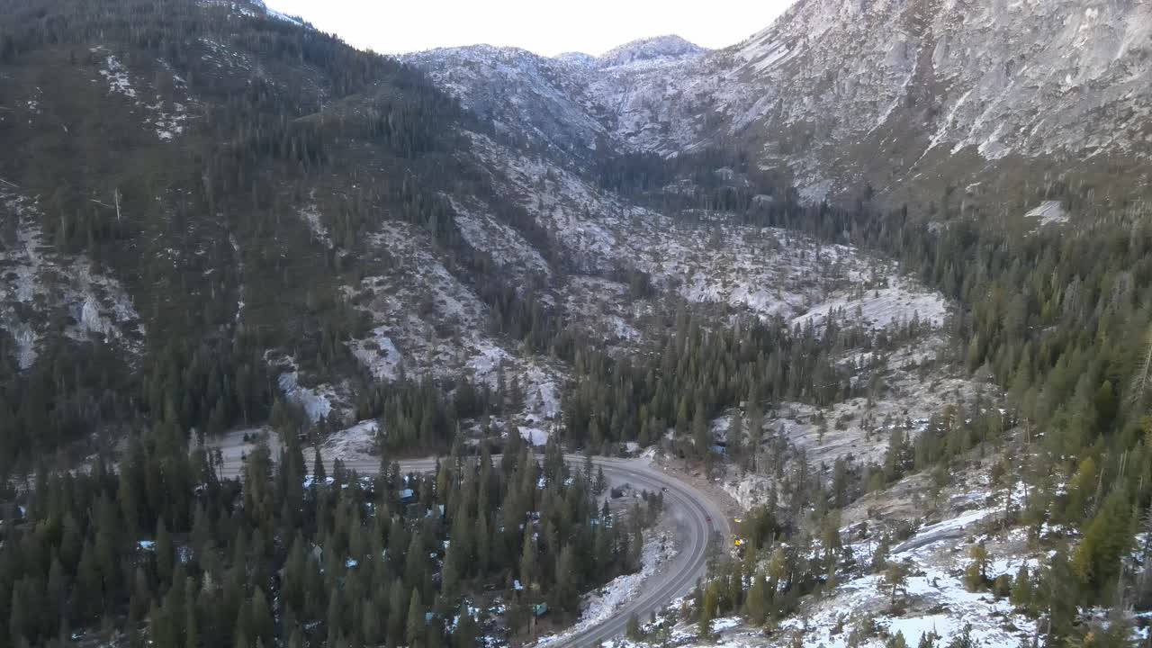 volando en un día de invierno cerca de una carretera asfaltada en un valle a la sombra de las montañas con pinos y nieve en el suelo