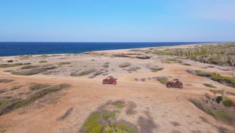 drone view of the rugged northern coast of curacao, utv riders cruise along dirt path highlighting the rocky terrain and dramatic shoreline