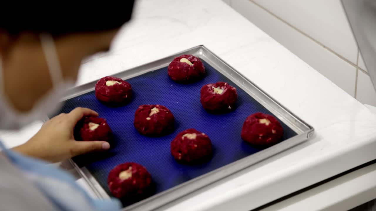 Red velvet cookie dough being placed on a pan for baking