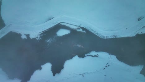 vista superior de una mujer bañándose en un río geotérmico en invierno en el valle de reykjadalur, en el sur de islandia
