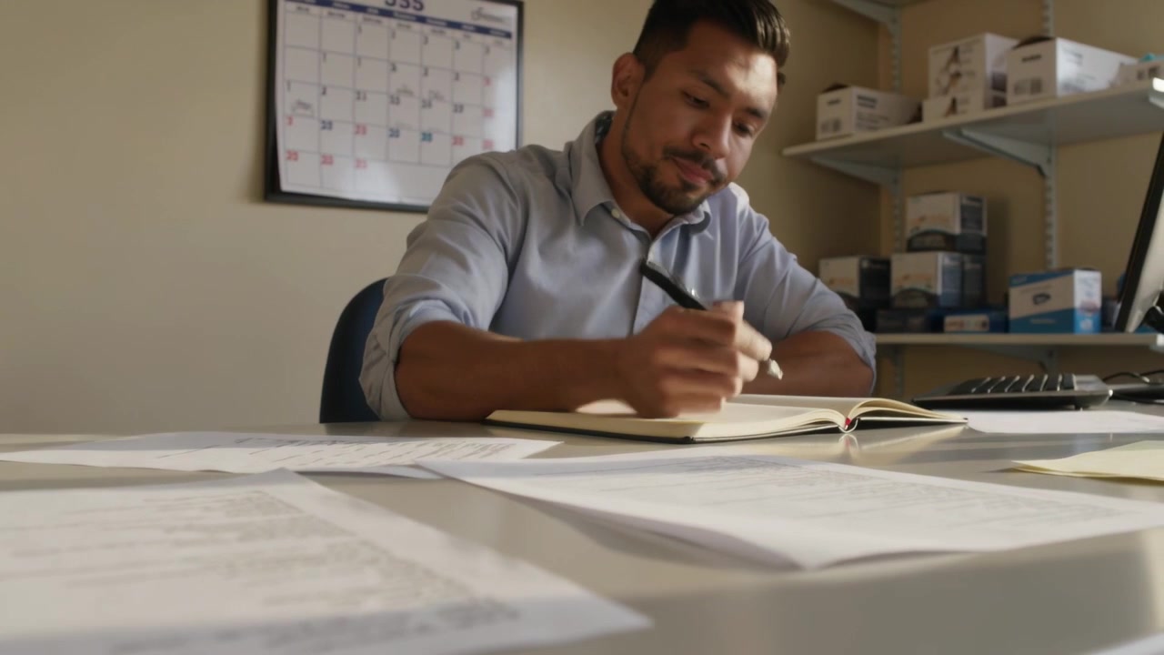 Holding sheet, office worker in blue shirt reading papers and writing work notes in notebook