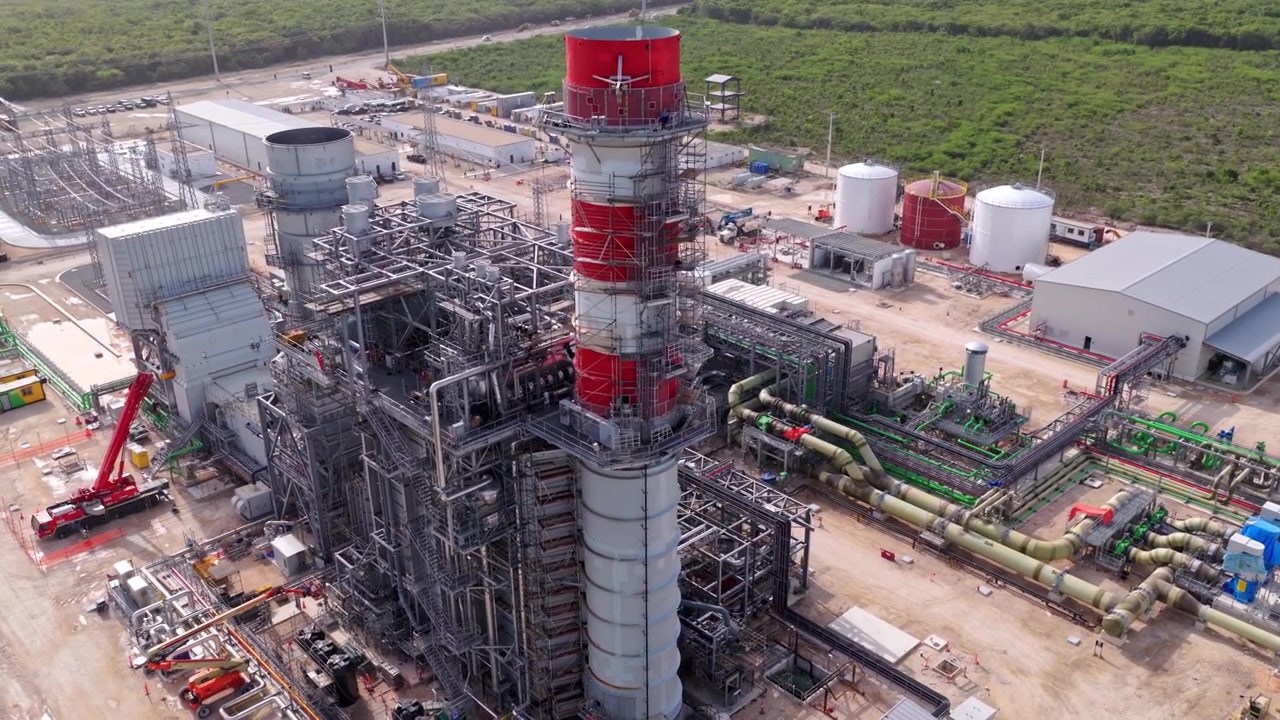 Vista aérea cercana de una moderna planta de energía mostrando grandes turbinas, chimeneas de escape, tuberías e infraestructura de ingeniería compleja en República Dominicana.
