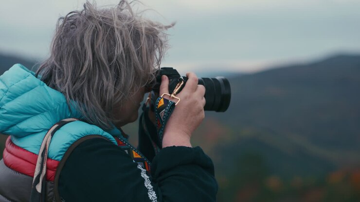 Cinematisk nærbillede af en kvindelig fotograf med gråt hår, der tager billeder med sit kamera på en blæsende dag i efterårsnaturen i slowmotion.
