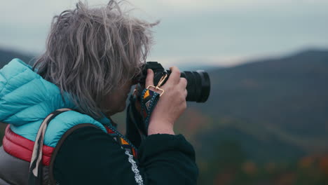 cinematic close up shot of a woman photographer with grey hair taking pictures with her camera during a windy day in autumn nature in slow motion