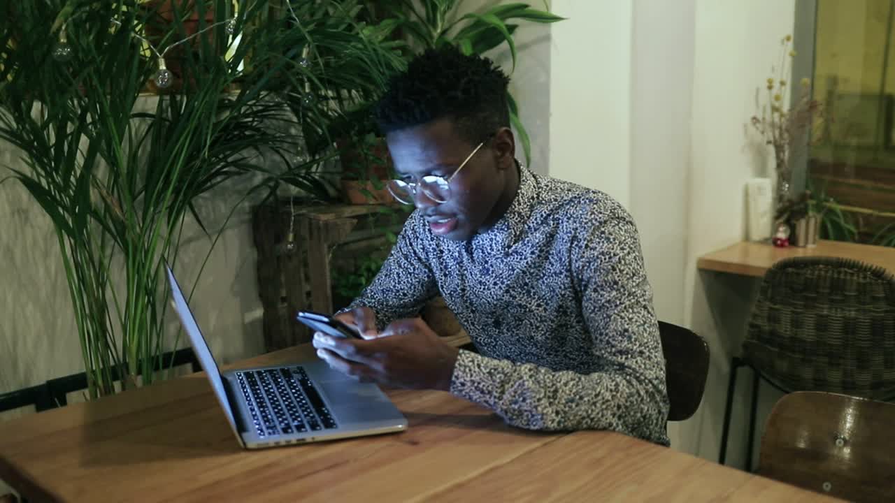 Cheerful young man using smartphone and laughing in cafe