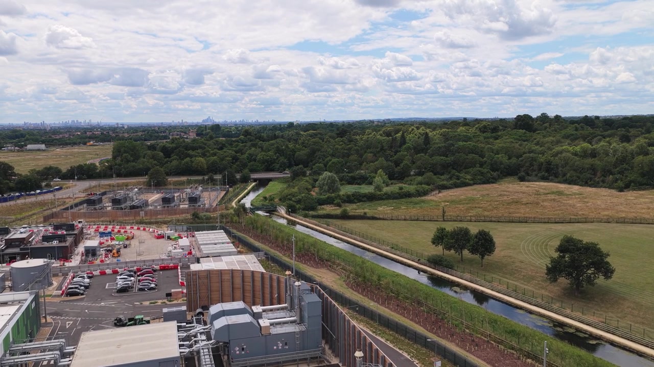 Prospettiva dall'alto di una centrale elettrica industriale circondata da campagna verde e prati sotto un cielo azzurro brillante con nuvole sparse durante un pomeriggio estivo soleggiato in Inghilterra.