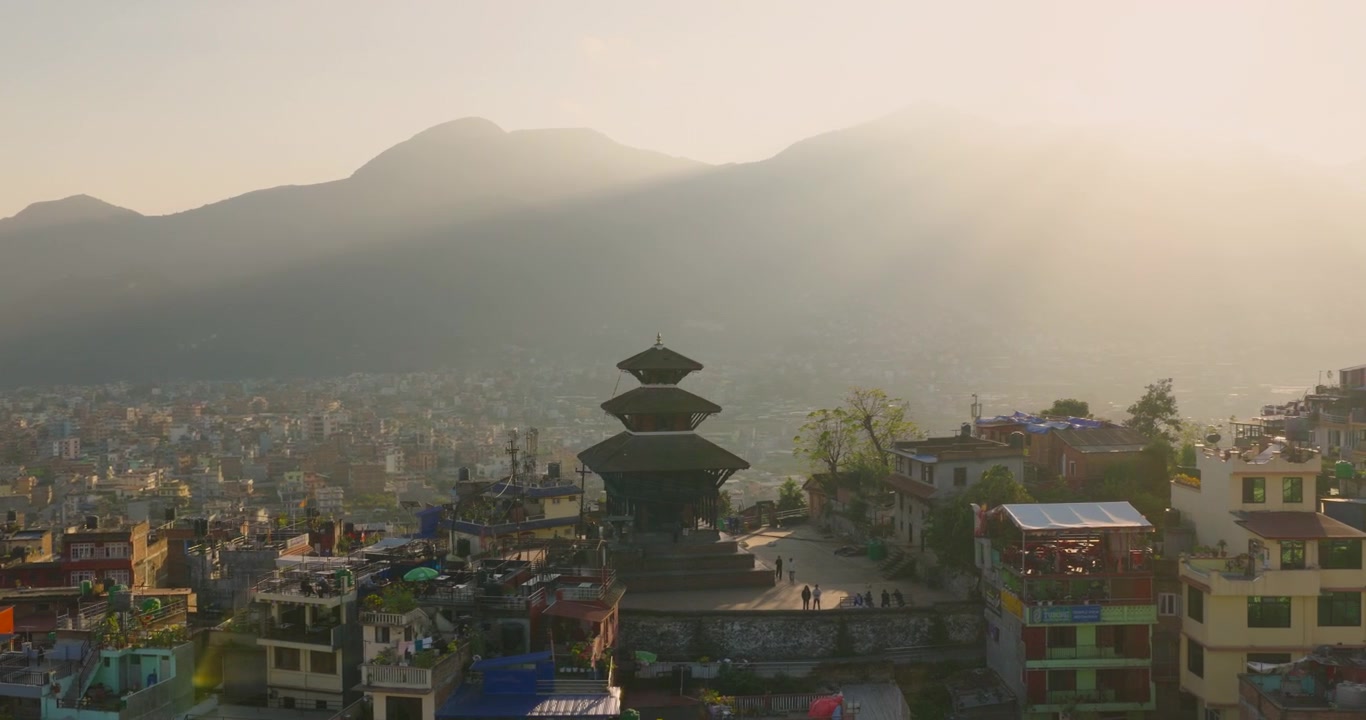 Kultaisen tunnin ilmakuva perinteisestä pagodityylisestä temppelistä Kirtipurissa, siluettina sumuisen Kathmandun laakson ja ympäröivien kukkuloiden taustalla auringonlaskun aikaan Nepalissa.
