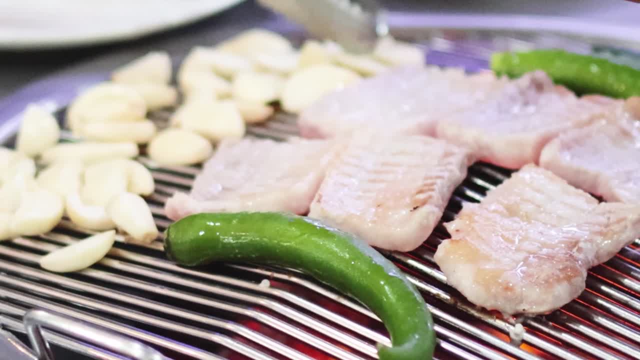 Vue rapprochée de poitrine de porc, d’ail et de poivrons verts en train de cuire sur un gril chaud