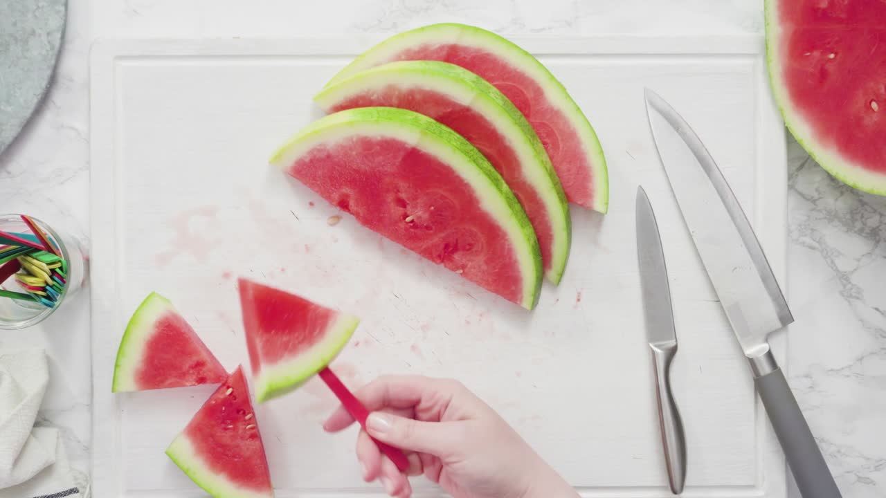 cortar la sandía roja en pedazos pequeños en una tabla de cortar blanca.