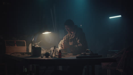 a bombmaker assembles a bomb in his workshop at night