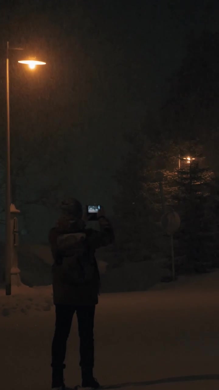 Uomo che scatta foto con il cellulare in un parco invernale di notte.
