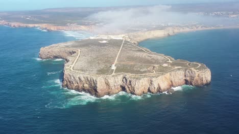 Cape-Sagres-Portugal-with-Sagres-Fortress-and-lighthouse-on-top-of-the-eroding-coast,-Aerial-dolly-out