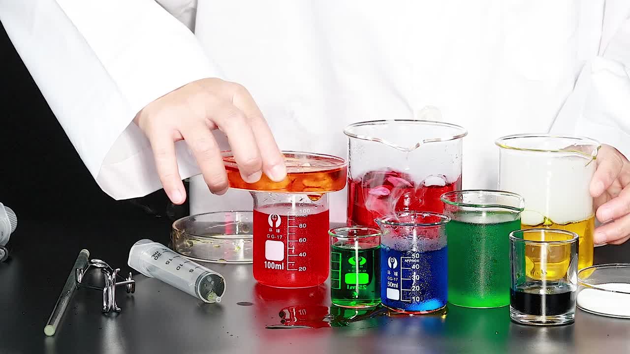A person in a lab coat mixes colorful liquids in various beakers on a lab table.