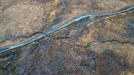 Glencoe's-rugged-terrain-with-natural-patterns-and-a-small-stream,-aerial-view