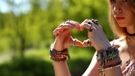 woman's hands adorned with bohemian jewelry forming a heart shape outdoors
