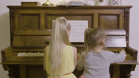 vista trasera de dos niñas tocando el piano viejo en casa