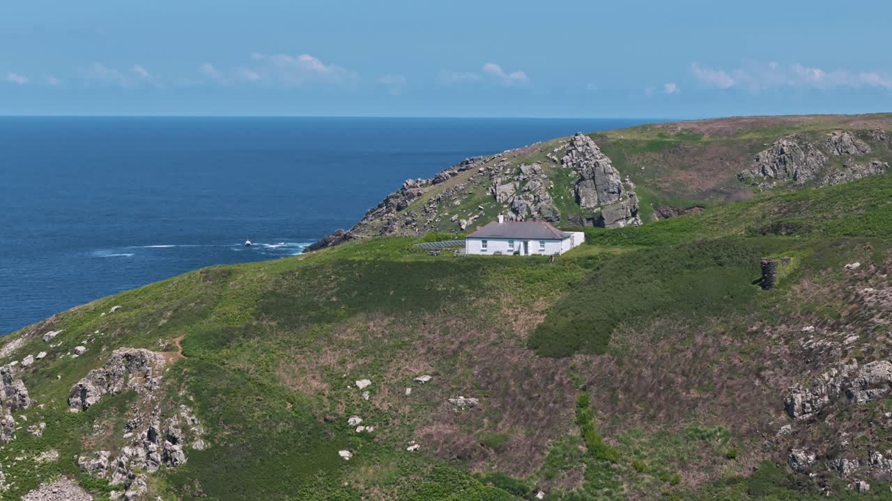 Flyover of a house perched above the sea on the cliffs of northern Cornwall with bright blue water and sunlit landscape
