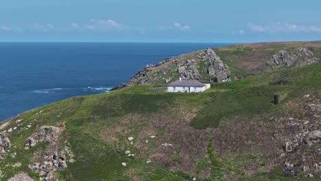 Flyover of a house perched above the sea on the cliffs of northern Cornwall with bright blue water and sunlit landscape
