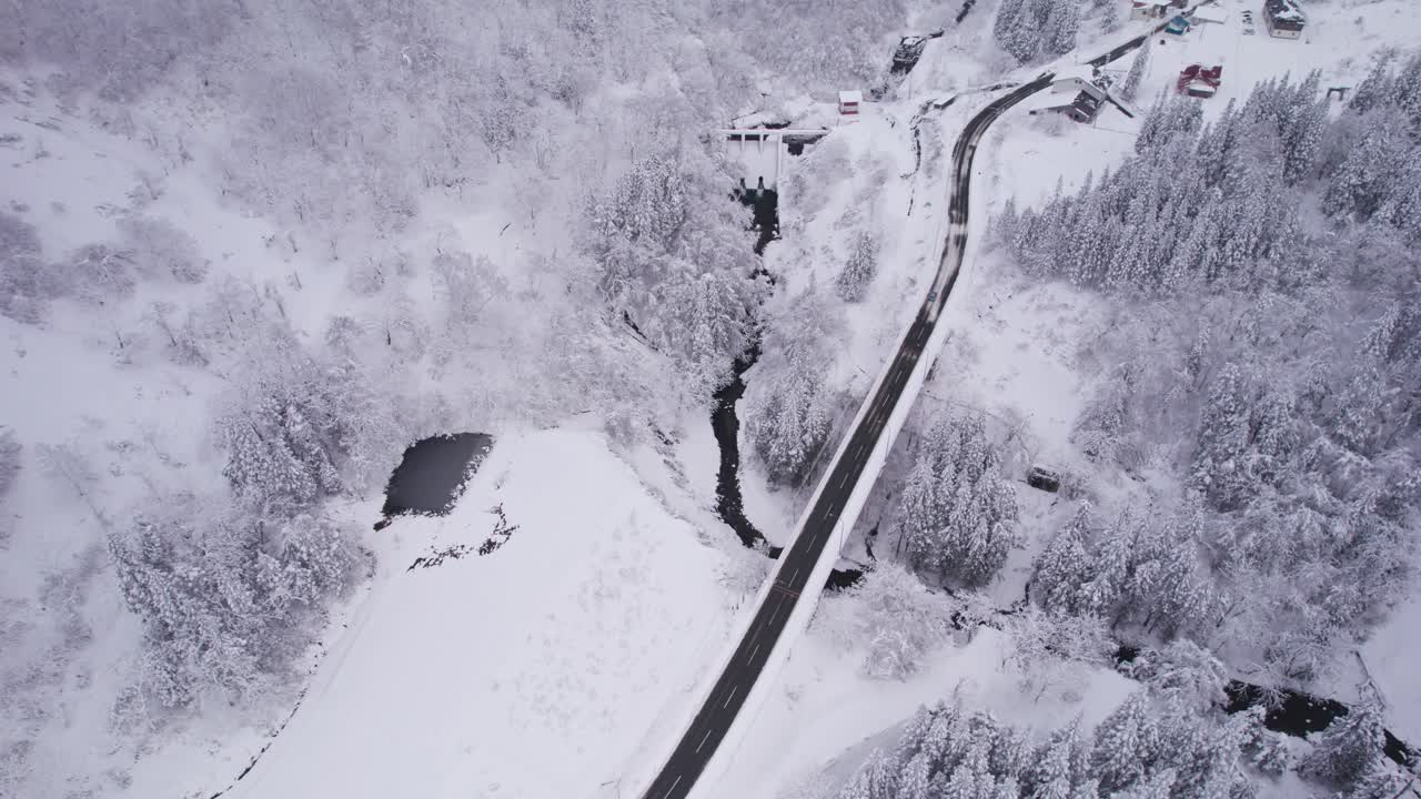 A cinematic aerial showing the quiet beauty of winter in Japan with roads, rivers, and snow-covered terrain