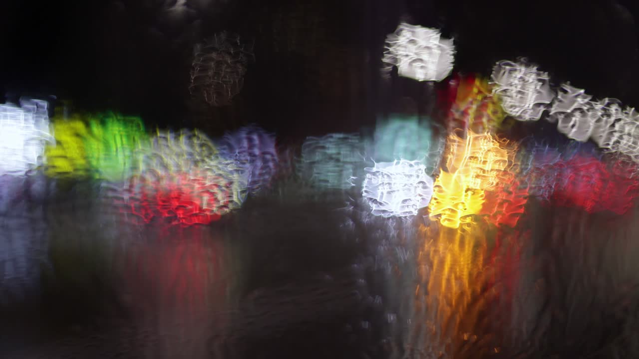 Abstract shot from the wet car window on the evening city traffic. Hopelessness, fatigue, loneliness concept. Rainy autumn weather. Slow motion 4K
