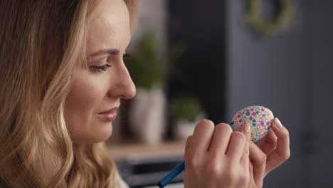 Close-up-side-view-of-cheerful-caucasian-woman-decorating-easter-eggs-in-the-domestic-kitchen.