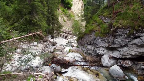 aerial dolly flying downstream a creek flowing through a mountain forest, descending view