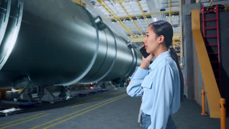 side view of asian business woman talking on mobile phone in pipe manufacturing factory