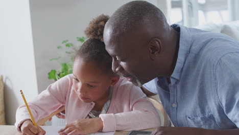 grandfather helping granddaughter with home schooling sitting at table with digital tablet