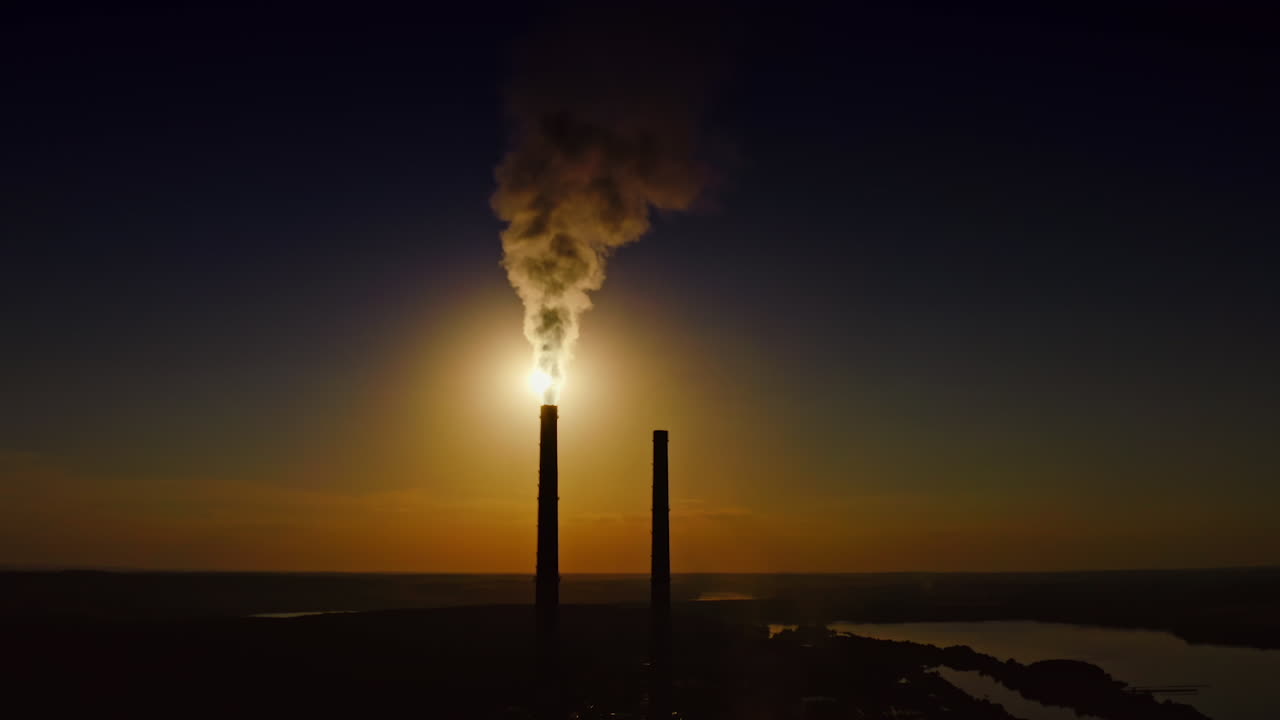 Massive smoke from stacks against the moon. Dark silhouette of industrial tower pipes at night. Thick fumes going into the air in the evening. Ecological disaster. Aerial view.