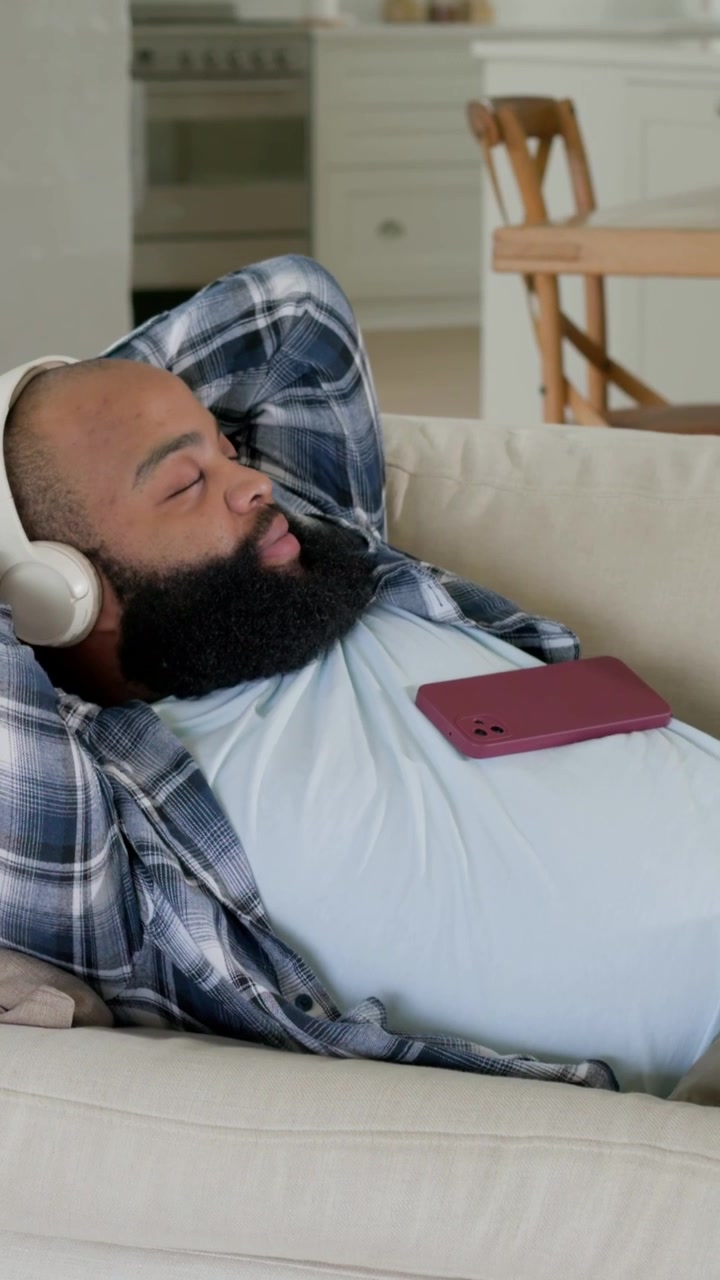 Vertikal video: Klip starter med mand, der læner sig tilbage på sofa iført headset, skifter position let, viser ro