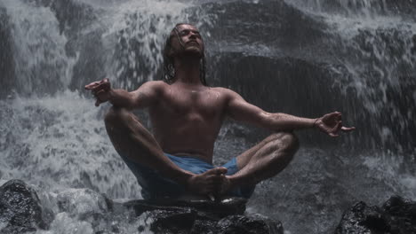 een jonge man die onder een waterval mediteert.