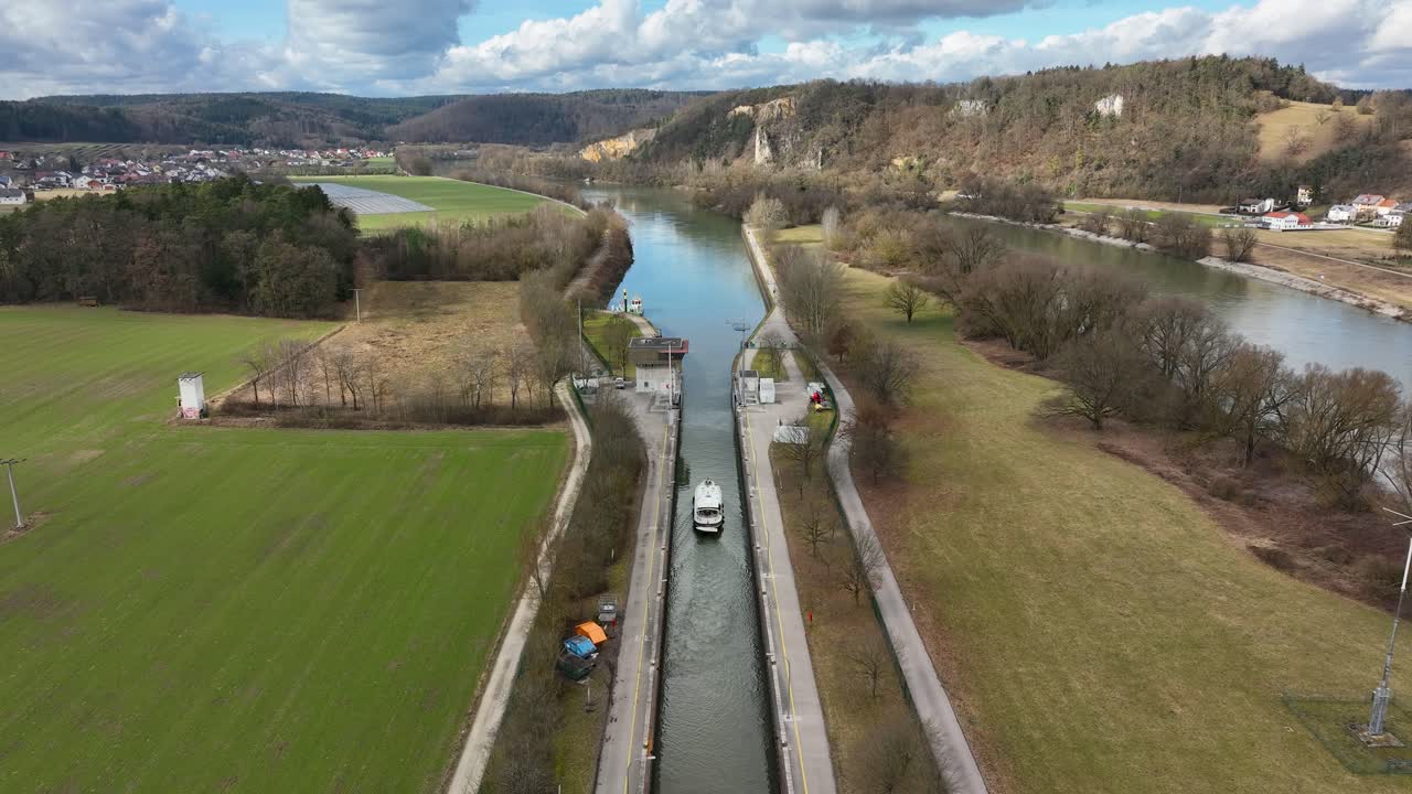 An aerial view of a boat in the middle of a lock system on the Danube Canal in Germany. Highlights the engineering of the waterway and the surrounding natural landscape