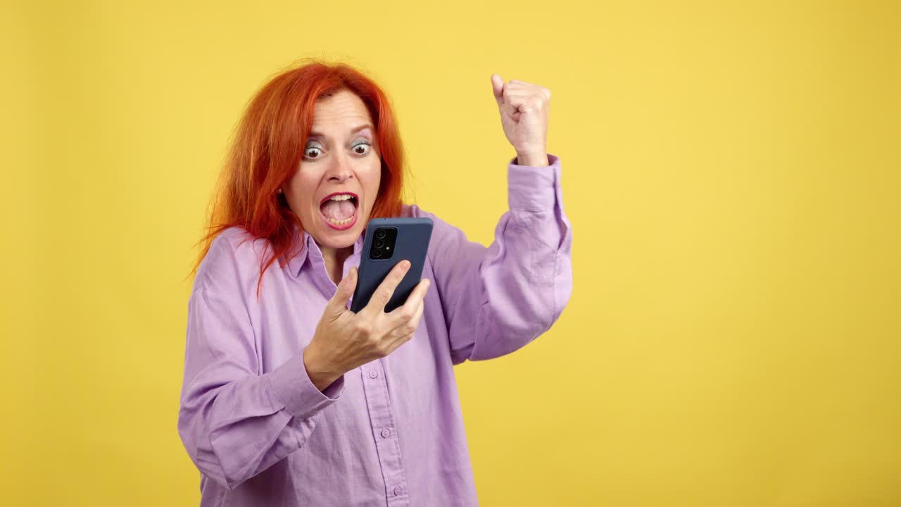 Excited red-haired woman celebrating success on her smartphone