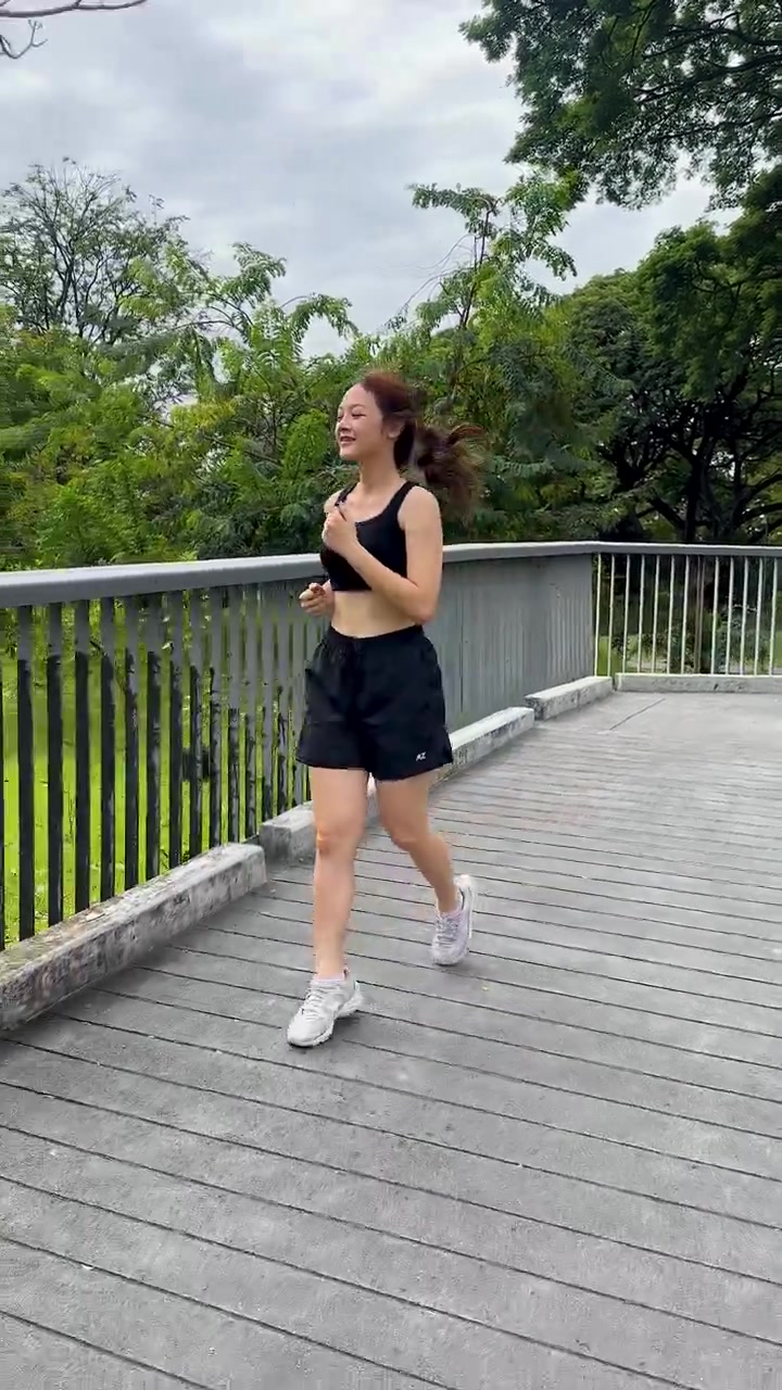 Una donna in forma in abbigliamento sportivo nero corre su un ponte circondato da alberi verdi del parco